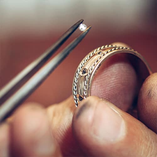 closeup of hands holding tweezers with a diamond and a gold ring