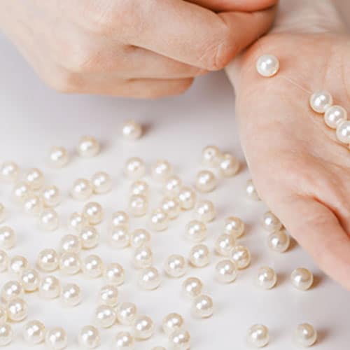 closeup of hands holding pearls with a bunch of pearls also scattered on the table below