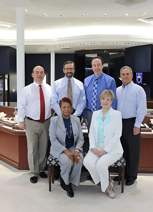 Morris Jewelers team standing in their showroom. 4 men are standing behind 2 women seated on a bench